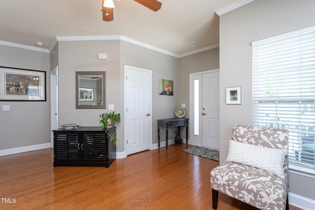 living area featuring wood finished floors, ceiling fan, crown molding, and baseboards