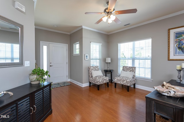 living area with wood finished floors, a ceiling fan, baseboards, and ornamental molding