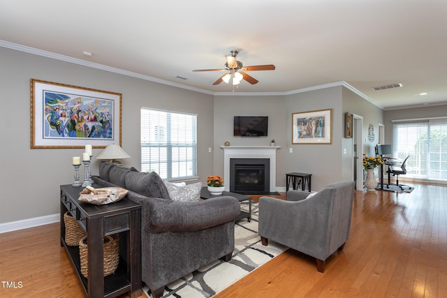 living area with a ceiling fan, light wood-style floors, a fireplace with flush hearth, crown molding, and baseboards