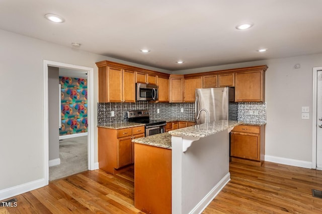 305 Freeman St, Raleigh, NC 27601 - kitchen with appliances with stainless steel finishes, light wood finished floors, brown cabinets, light stone counters, and recessed lighting