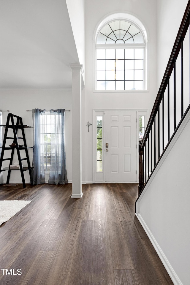 entryway featuring dark wood-style floors, decorative columns, stairway, healthy amount of natural light, and a high ceiling