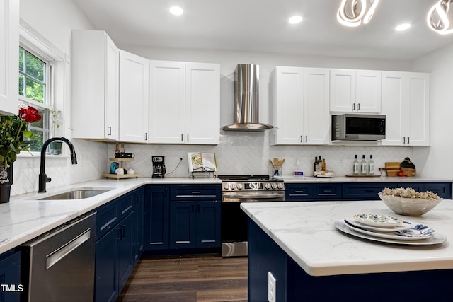 kitchen featuring wall chimney exhaust hood, stainless steel appliances, a sink, blue cabinets, and recessed lighting