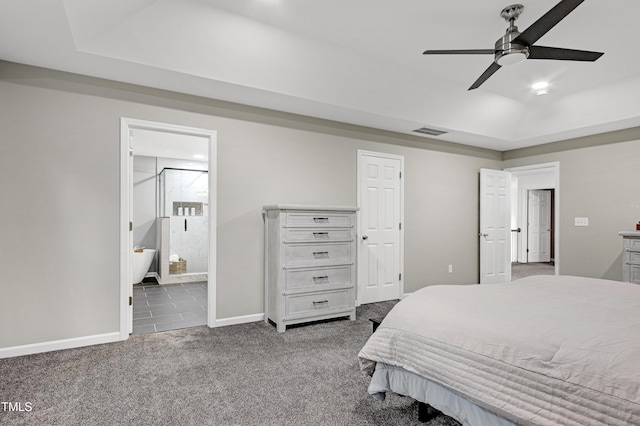 bedroom featuring dark colored carpet, a tray ceiling, baseboards, ensuite bath, and a ceiling fan