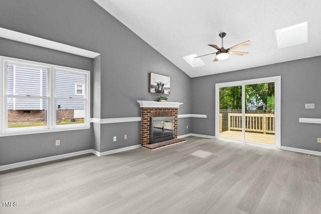 2402 Cynthia Dr, Durham, NC 27704 - unfurnished living room featuring baseboards, vaulted ceiling with skylight, a ceiling fan, a brick fireplace, and wood finished floors