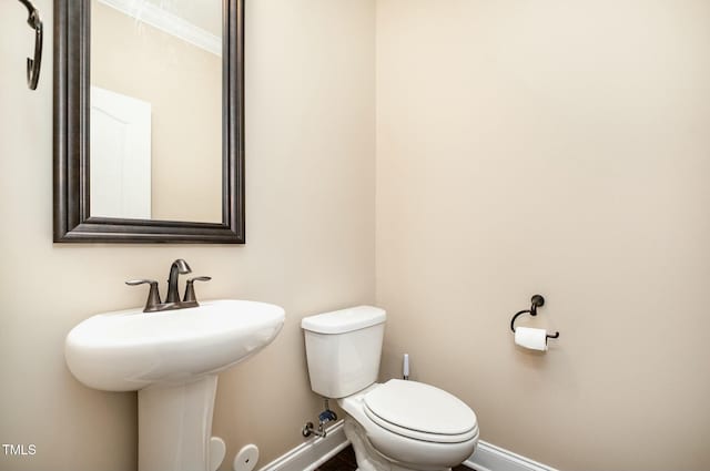 half bath featuring baseboards, toilet, and a sink