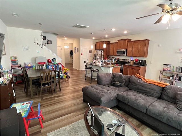 living area featuring light wood finished floors, visible vents, recessed lighting, ceiling fan with notable chandelier, and stairs