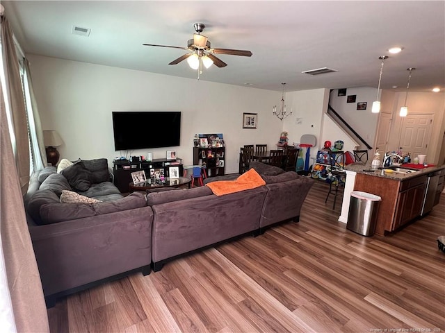 living room with ceiling fan with notable chandelier, wood finished floors, and visible vents