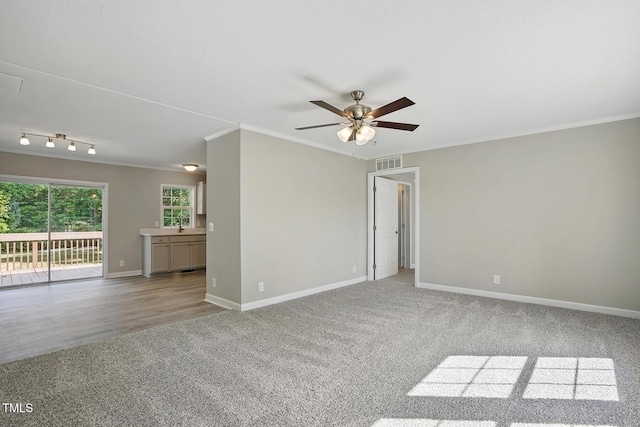 empty room with carpet flooring, crown molding, ceiling fan, baseboards, and visible vents