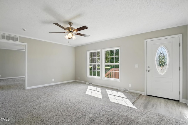 entryway featuring crown molding, a ceiling fan, a textured ceiling, and visible vents
