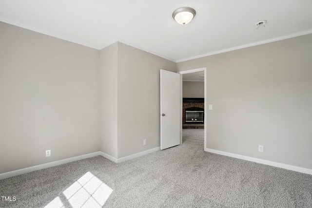 spare room featuring crown molding, carpet flooring, baseboards, and a brick fireplace