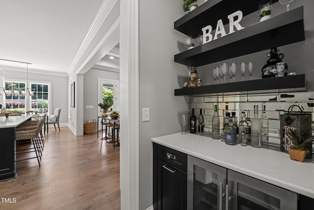 bar with crown molding, wood finished floors, baseboards, a bar, and wine cooler