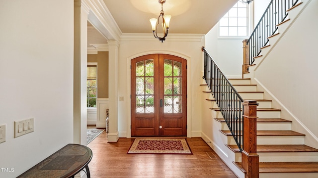 foyer entrance with stairway, wood finished floors, french doors, crown molding, and a chandelier
