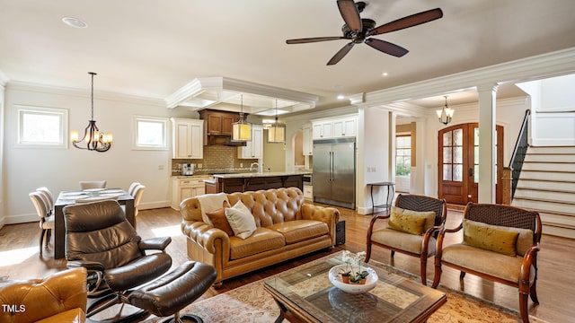 living area with ornamental molding, a chandelier, light wood-style floors, a ceiling fan, and stairs
