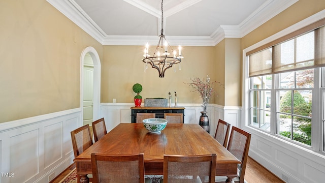 dining area featuring a decorative wall, ornamental molding, a wainscoted wall, a chandelier, and arched walkways