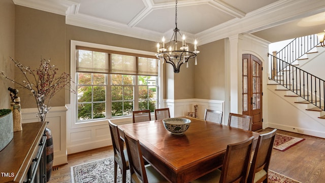 dining room featuring light wood-style floors, stairway, crown molding, a decorative wall, and coffered ceiling
