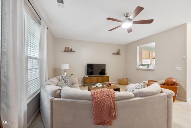 living area featuring baseboards, visible vents, light carpet, and ceiling fan