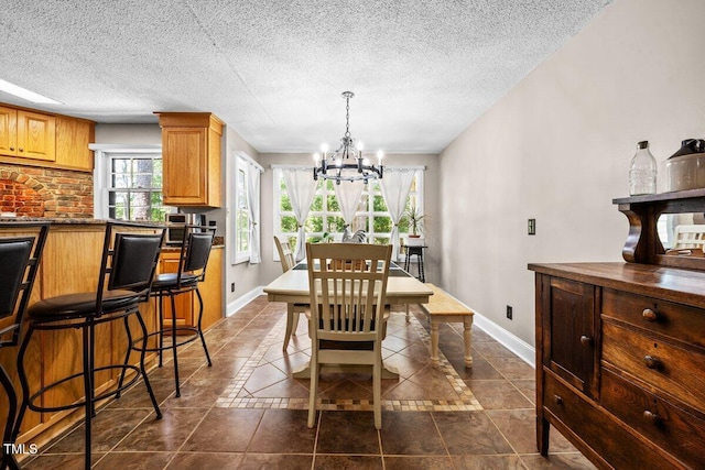dining room featuring an inviting chandelier, baseboards, dark tile patterned floors, and a textured ceiling