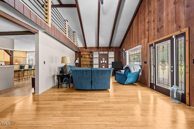 living area with wooden walls, high vaulted ceiling, light wood-type flooring, and beam ceiling