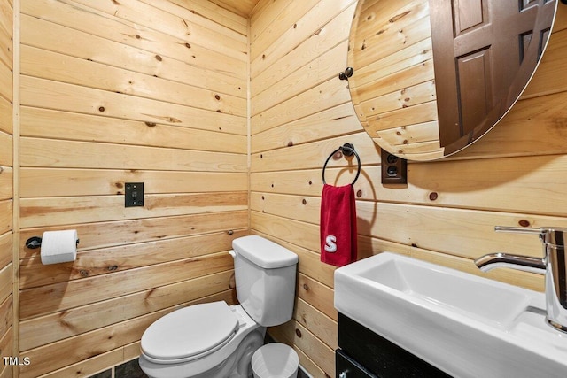 bathroom featuring a sink, wooden walls, and toilet