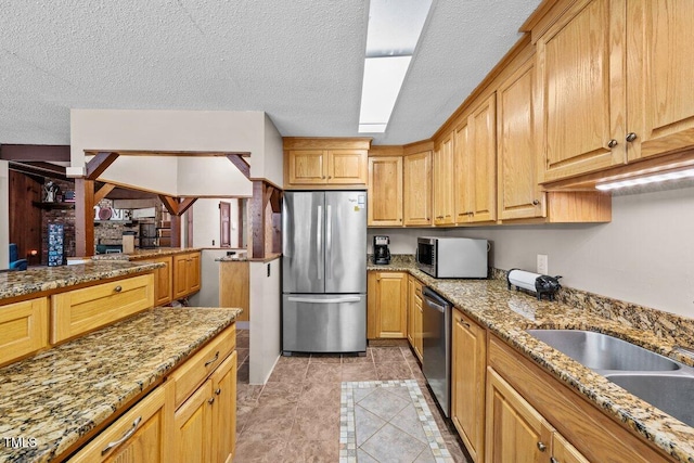 kitchen featuring light tile patterned floors, appliances with stainless steel finishes, light stone countertops, and a sink