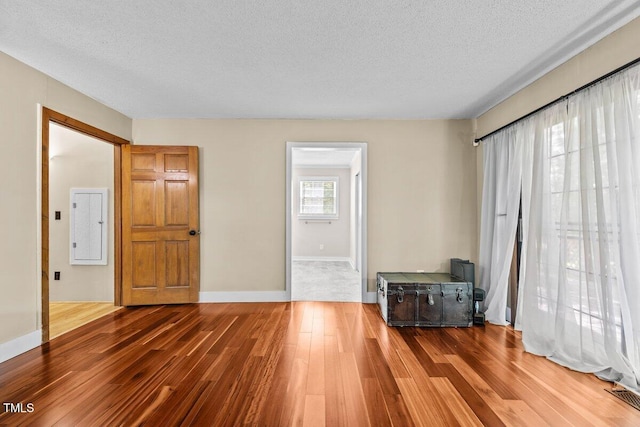 unfurnished living room featuring a textured ceiling, baseboards, wood finished floors, visible vents, and electric panel