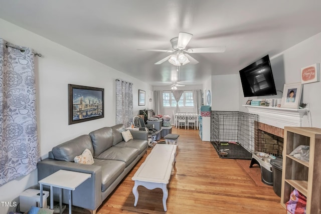 living area featuring a ceiling fan, wood finished floors, and a fireplace