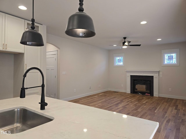 kitchen featuring a sink, ceiling fan, wood finished floors, light stone counters, and white cabinetry