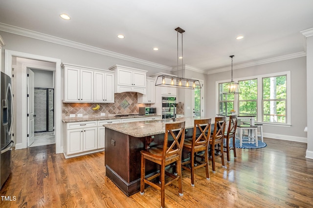 kitchen featuring light stone countertops, decorative backsplash, a kitchen island with sink, and white cabinets