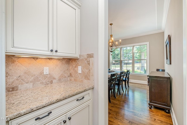 kitchen with light stone countertops, a chandelier, crown molding, decorative backsplash, and wood finished floors