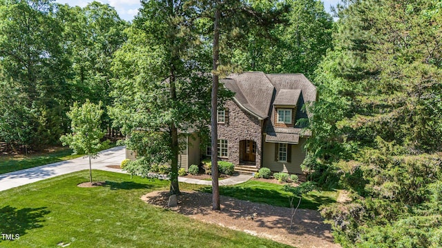 tudor house with concrete driveway, stone siding, and a front yard