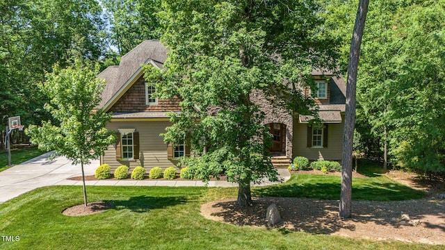view of property hidden behind natural elements featuring a front lawn, concrete driveway, and roof with shingles