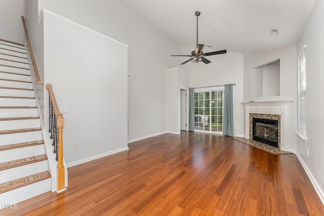 unfurnished living room with wood finished floors, a fireplace, baseboards, ceiling fan, and stairway