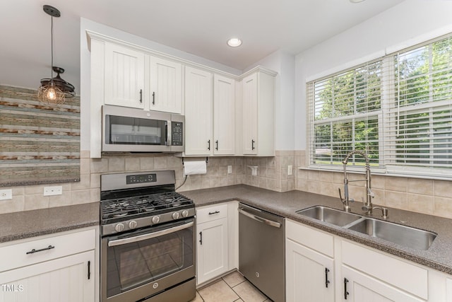 kitchen featuring backsplash, dark countertops, a sink, stainless steel appliances, and white cabinetry