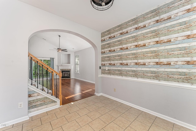 tiled spare room with arched walkways, ceiling fan, baseboards, and a fireplace