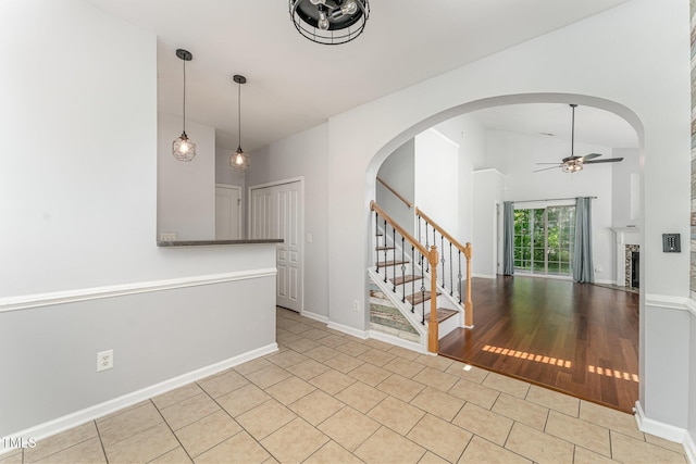 tiled spare room with ceiling fan, a fireplace, arched walkways, baseboards, and stairway