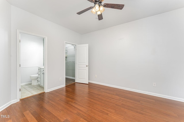 unfurnished bedroom featuring a walk in closet, ensuite bath, baseboards, wood finished floors, and a closet