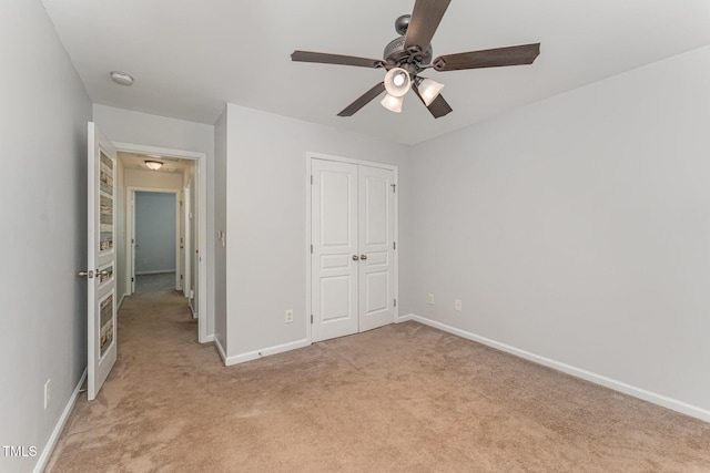 unfurnished bedroom with baseboards, ceiling fan, a closet, and light colored carpet