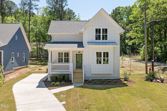 view of front facade featuring a shingled roof, covered porch, board and batten siding, and a front yard