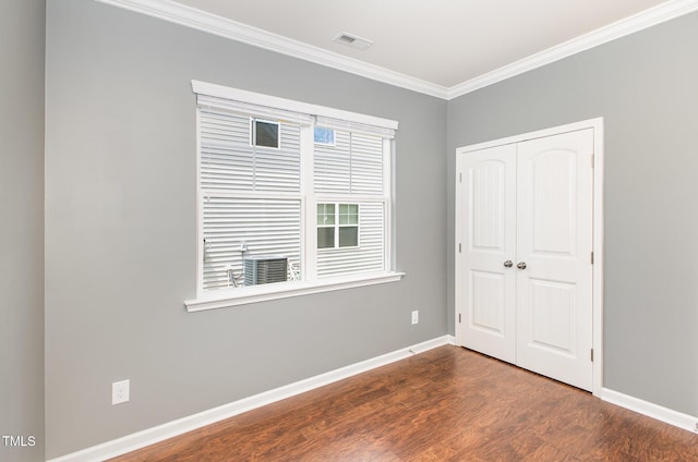 empty room with dark wood-style flooring, visible vents, baseboards, and ornamental molding