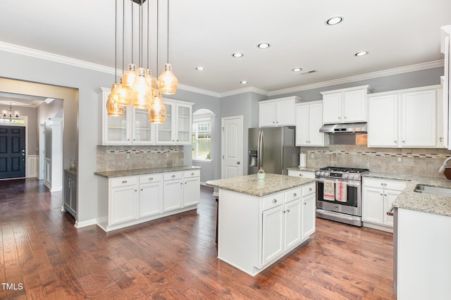 kitchen with stainless steel appliances, white cabinetry, a chandelier, under cabinet range hood, and ornamental molding