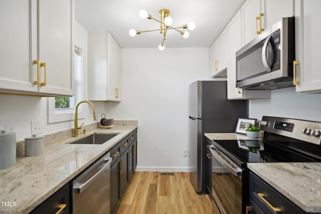 kitchen featuring appliances with stainless steel finishes, a sink, light wood finished floors, and white cabinetry