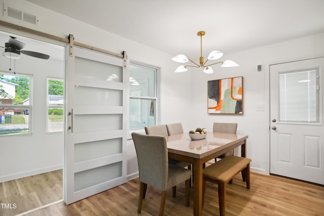 dining room featuring light wood-style flooring, a chandelier, a barn door, and baseboards