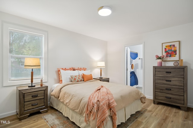 bedroom with light wood-type flooring, baseboards, and a walk in closet
