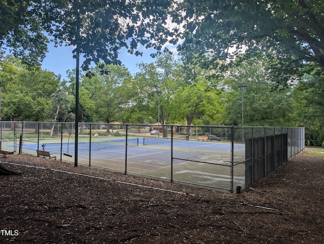 view of tennis court featuring fence and view of scattered trees