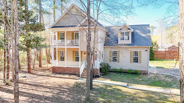view of front of home with fence, covered porch, a balcony, and a shingled roof