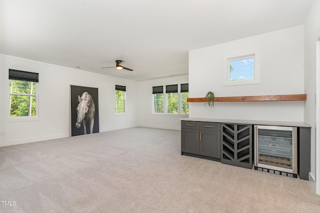 unfurnished living room featuring carpet floors, beverage cooler, baseboards, ceiling fan, and a bar