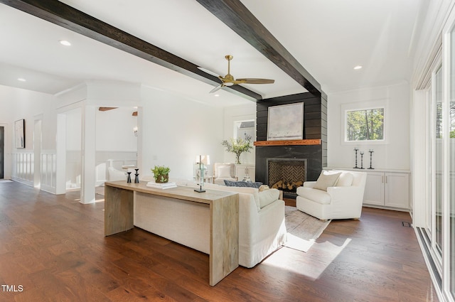 living area with a ceiling fan, beamed ceiling, dark wood finished floors, and a fireplace