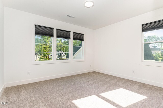 spare room with baseboards, visible vents, and light carpet