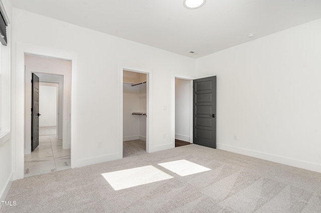 unfurnished bedroom featuring a walk in closet, baseboards, carpet, and a closet