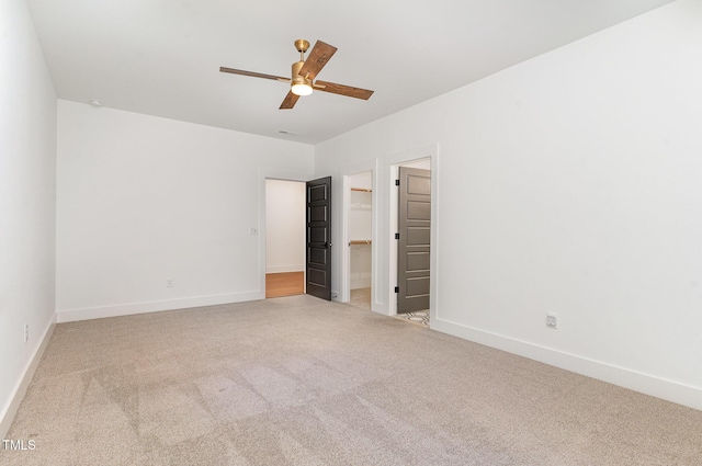 unfurnished bedroom with carpet floors, baseboards, a ceiling fan, and a walk in closet
